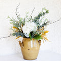 Floral bouquet in gold vase with white rose-style blooms, greenery, and berry twigs