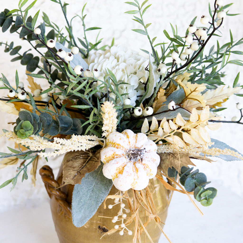 Floral bouquet close-up in gold vase with white blossoms, eucalyptus leaves, and pale gold accents