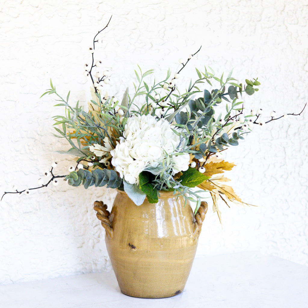 Floral bouquet in gold urn with white blossoms, green leaves, and golden accent foliage