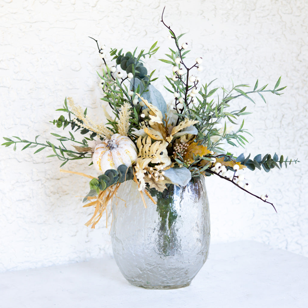 Floral bouquet in silver vase with cream-and-gold blooms, pine greenery, and white berry stems