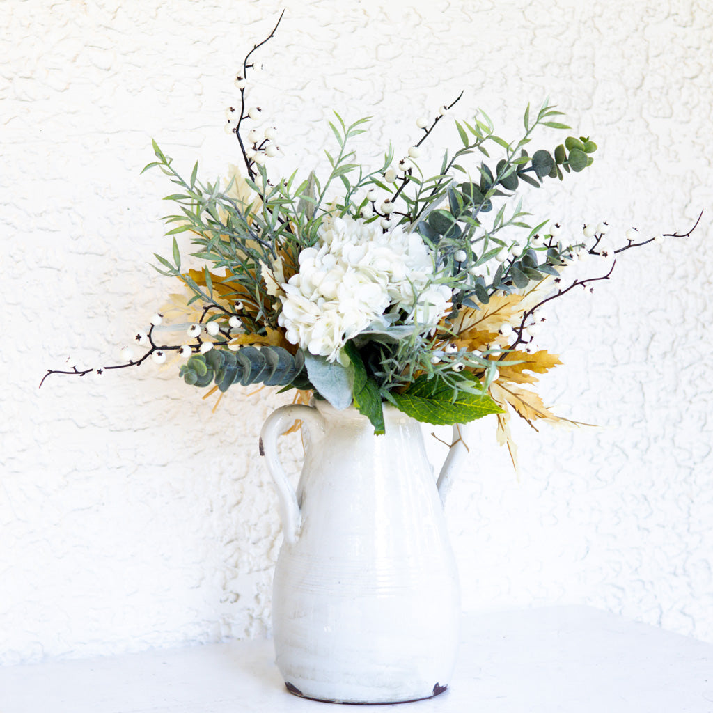 Floral bouquet in white vase with white rose blooms, eucalyptus, and golden foliage