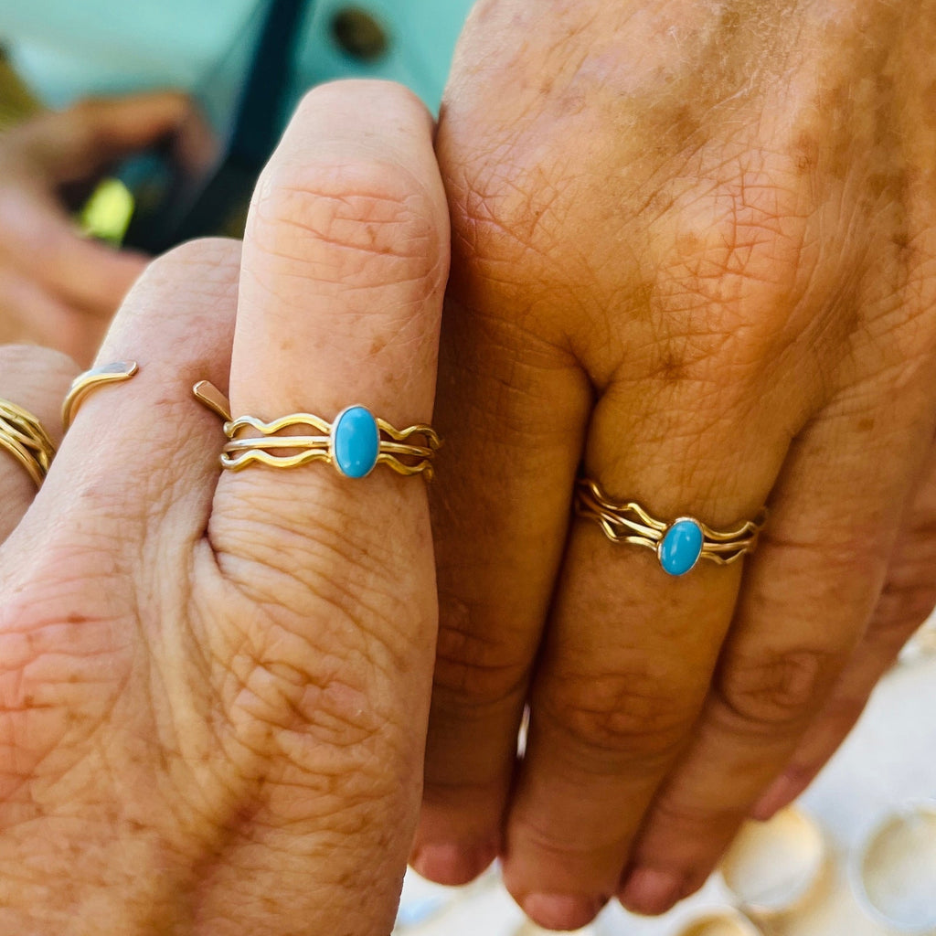 Gold-tone wave ring with oval turquoise cabochon, shown on two fingers