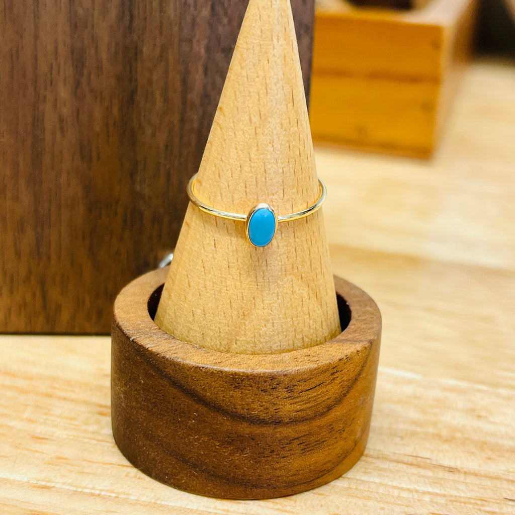 Gold-tone ring with oval turquoise cabochon on slim band, on a ring stand