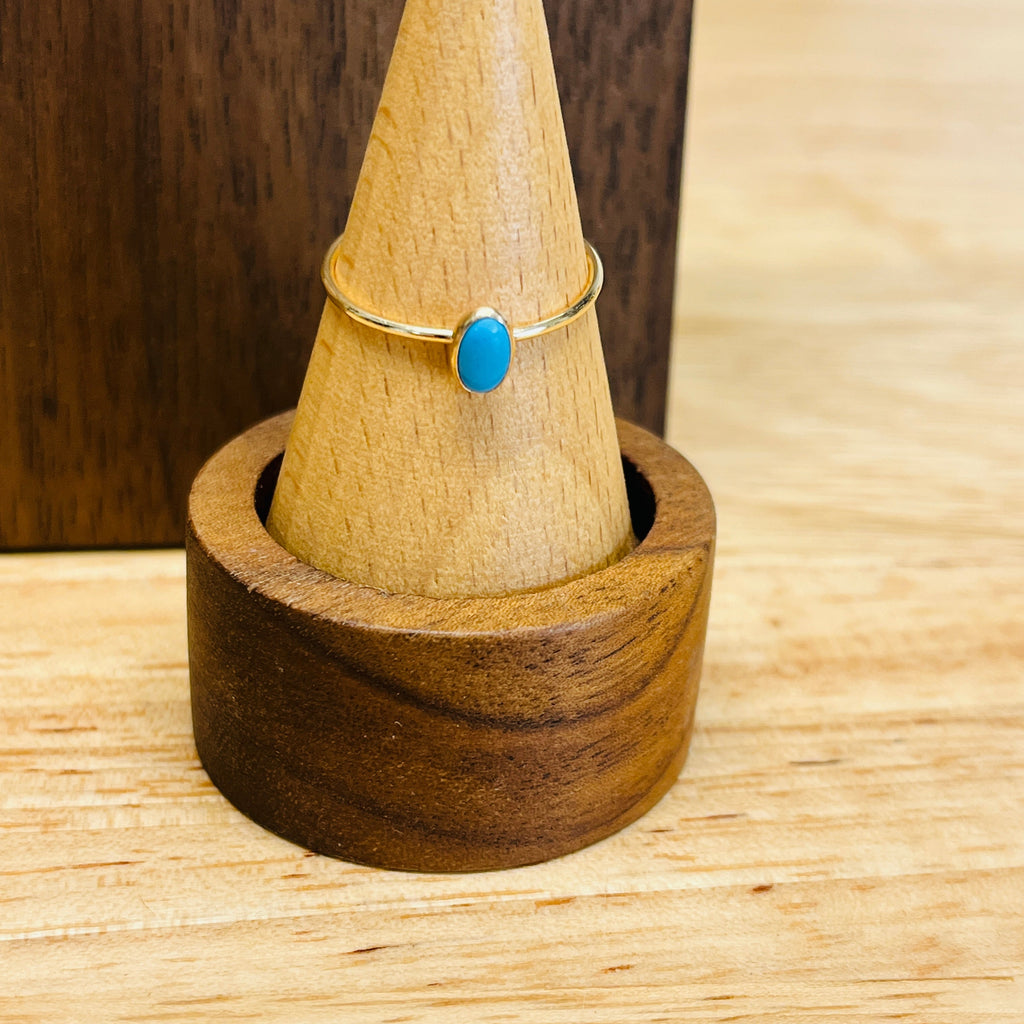 Gold-tone ring with oval turquoise cabochon on slim band, on a ring stand
