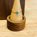 Gold-tone ring with oval turquoise cabochon on slim band, on a ring stand