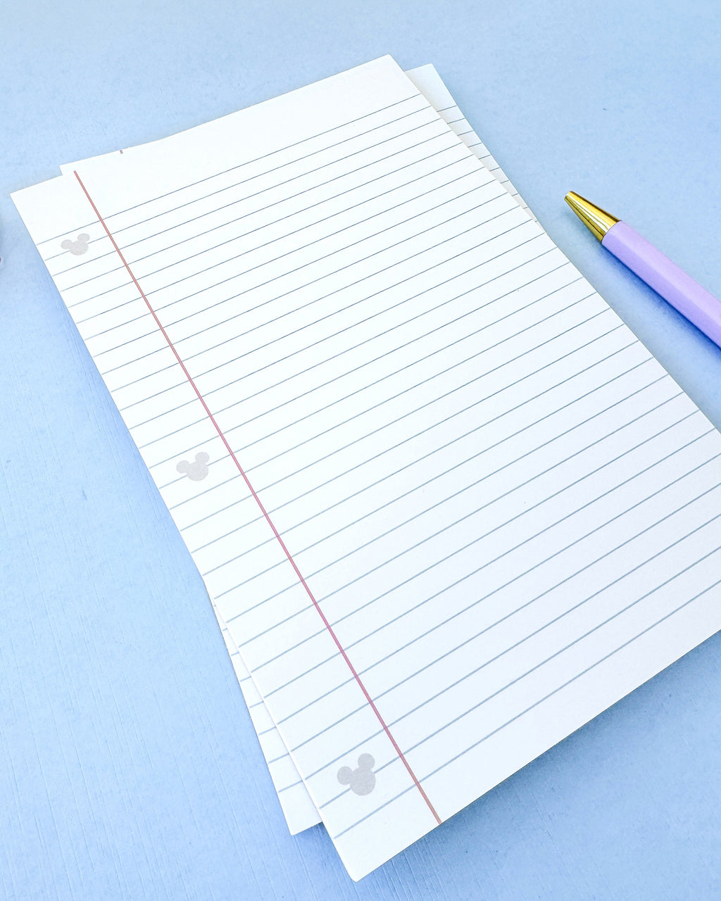 Stack of lined paper notepad sheets with red margin line and hidden Mickey icon border