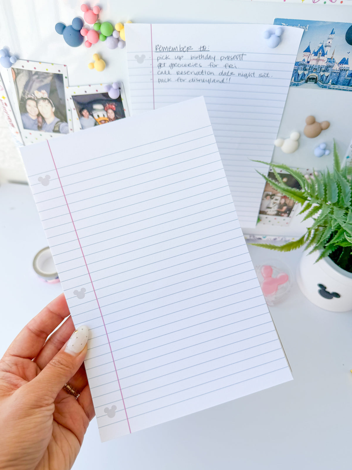 Lined paper notepad sheet held in hand, with red margin line and hidden Mickey icons