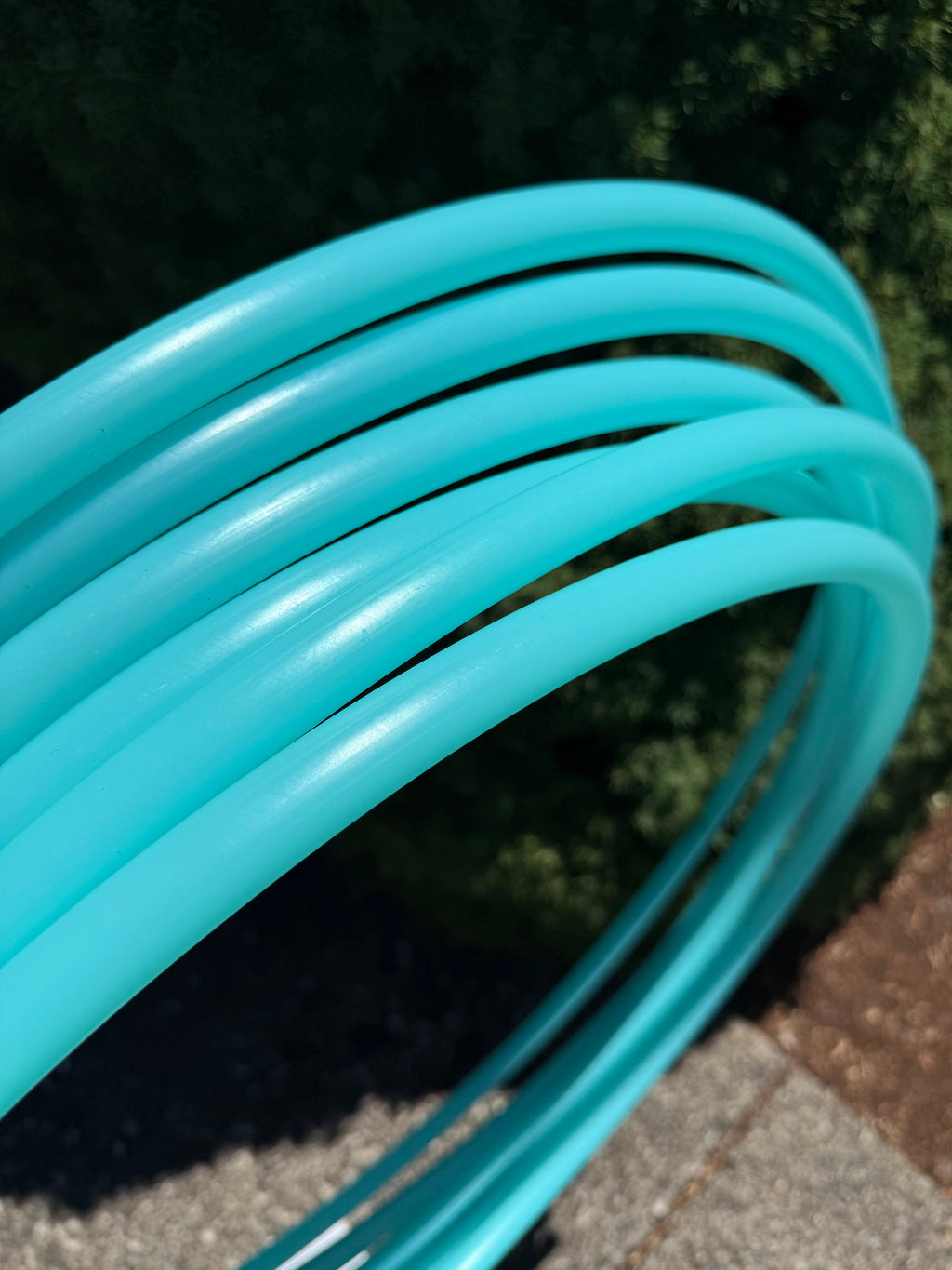 Teal aqua sea glass hoop tubing coiled on pavement, close-up of loops