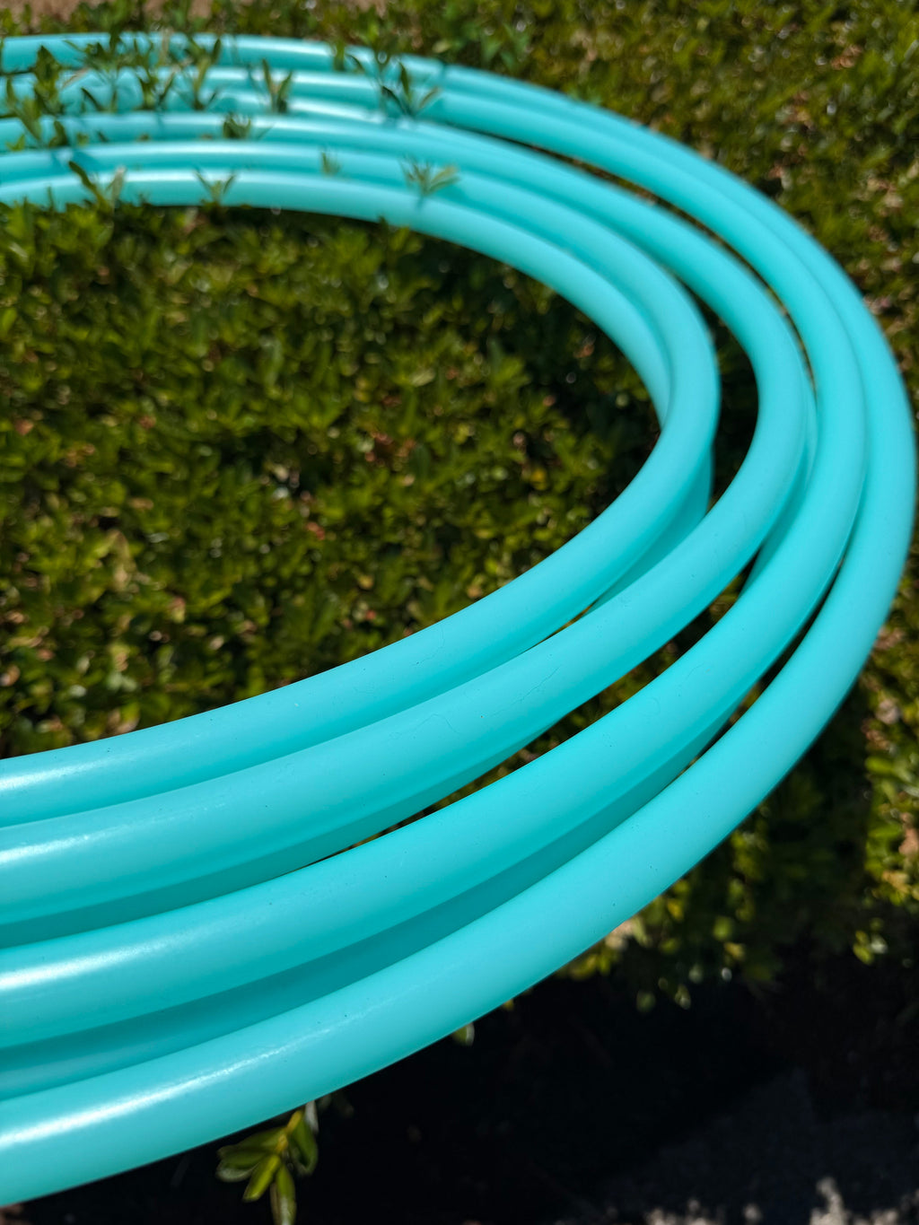 Aqua sea glass hoop tubing, teal coil in parallel loops outdoors close-up