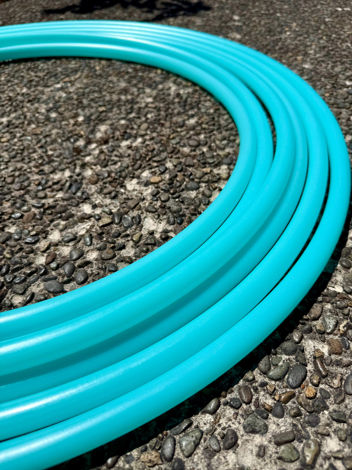 Aqua sea glass hoop tubing, teal coil on rough asphalt surface close-up