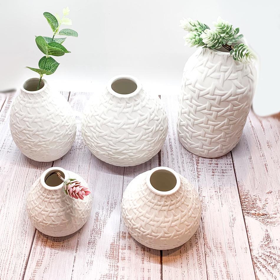 Five white web-pattern vases with open tops, arranged on a light wood surface