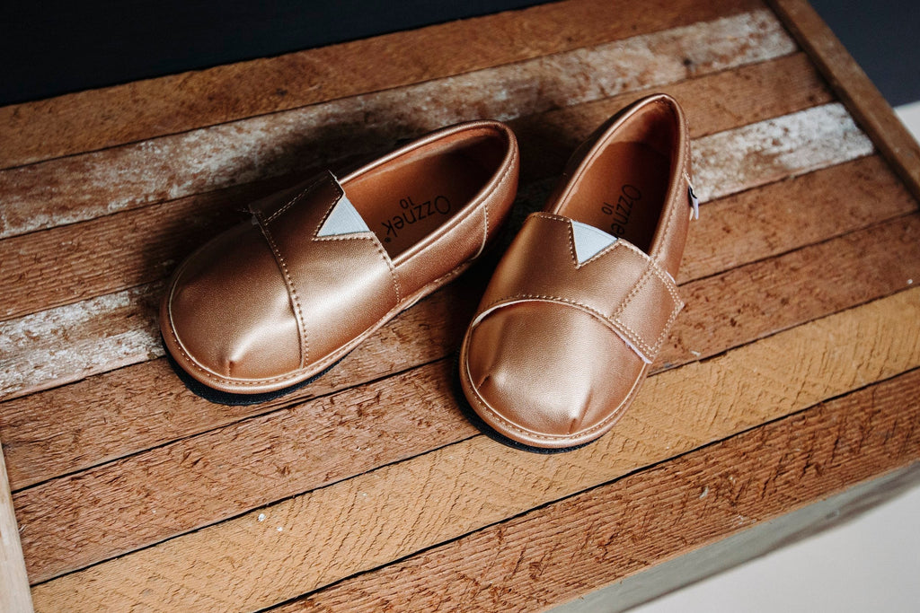 Gold metallic slip-on shoe topper pair on wooden floor with stitched strap panel