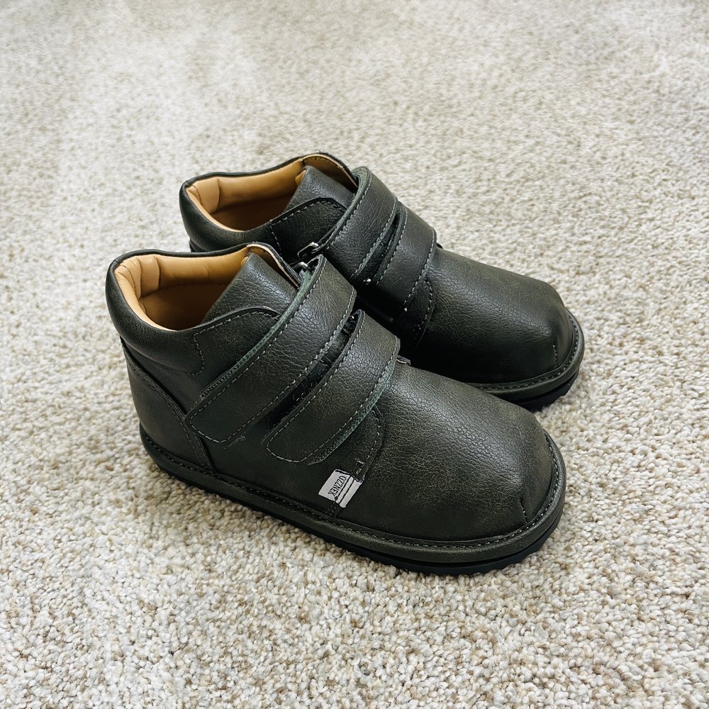 Pair of toddler barefoot sneakers in dark green on a carpet, side view.