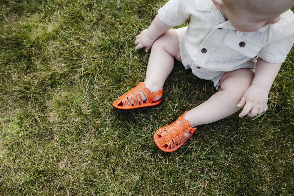 Orange kids sandals on grass, open-toe with adjustable hook-and-loop straps