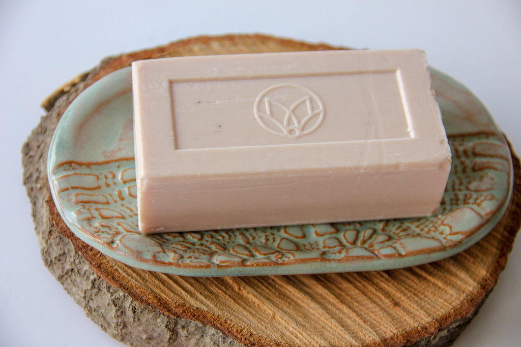 Ceramic soap dish tray with textured leaf pattern, holding an embossed white soap bar