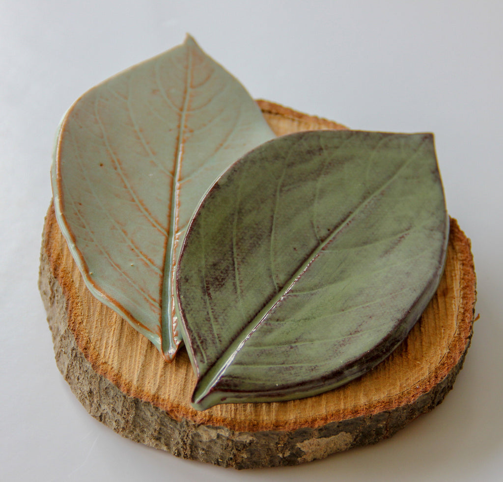 Stacked leaf-shaped dishes in moss green and oyster shell on a wood slice base