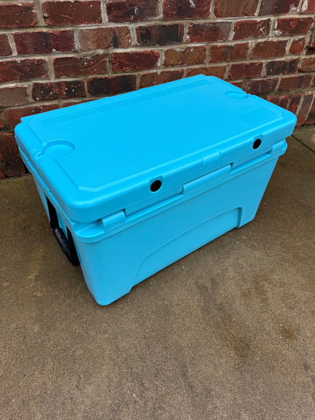 Light blue hard cooler with rear vent ports and black rubber wheel feet