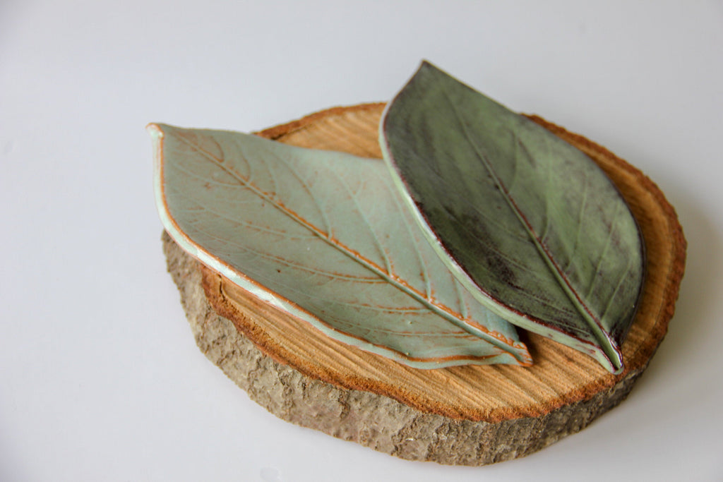 Pair of leaf-shaped dishes in dark green and pale oyster shell on a wood slice