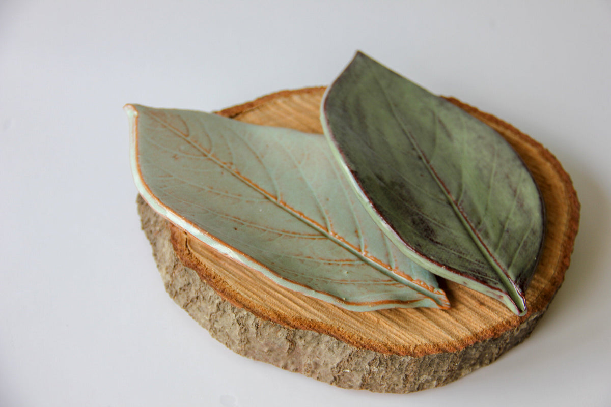 Pair of leaf-shaped dishes in dark green and pale oyster shell on a wood slice