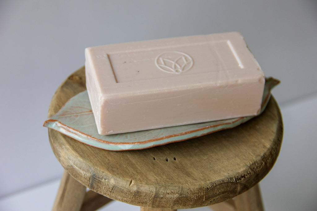 Leaf-shaped dish holding a white bar of soap on a wood slice