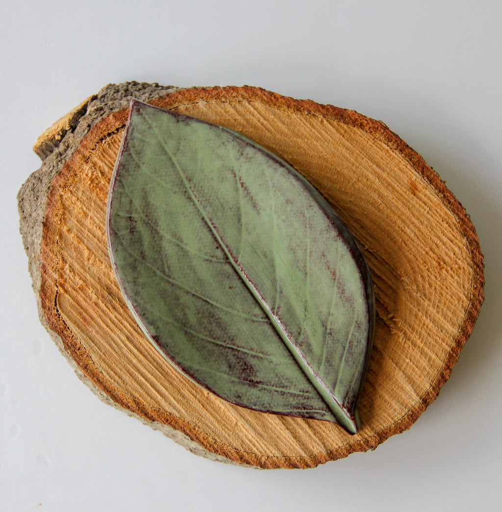 Moss green leaf-shaped dish on a rustic wood slice with red-stitch detail