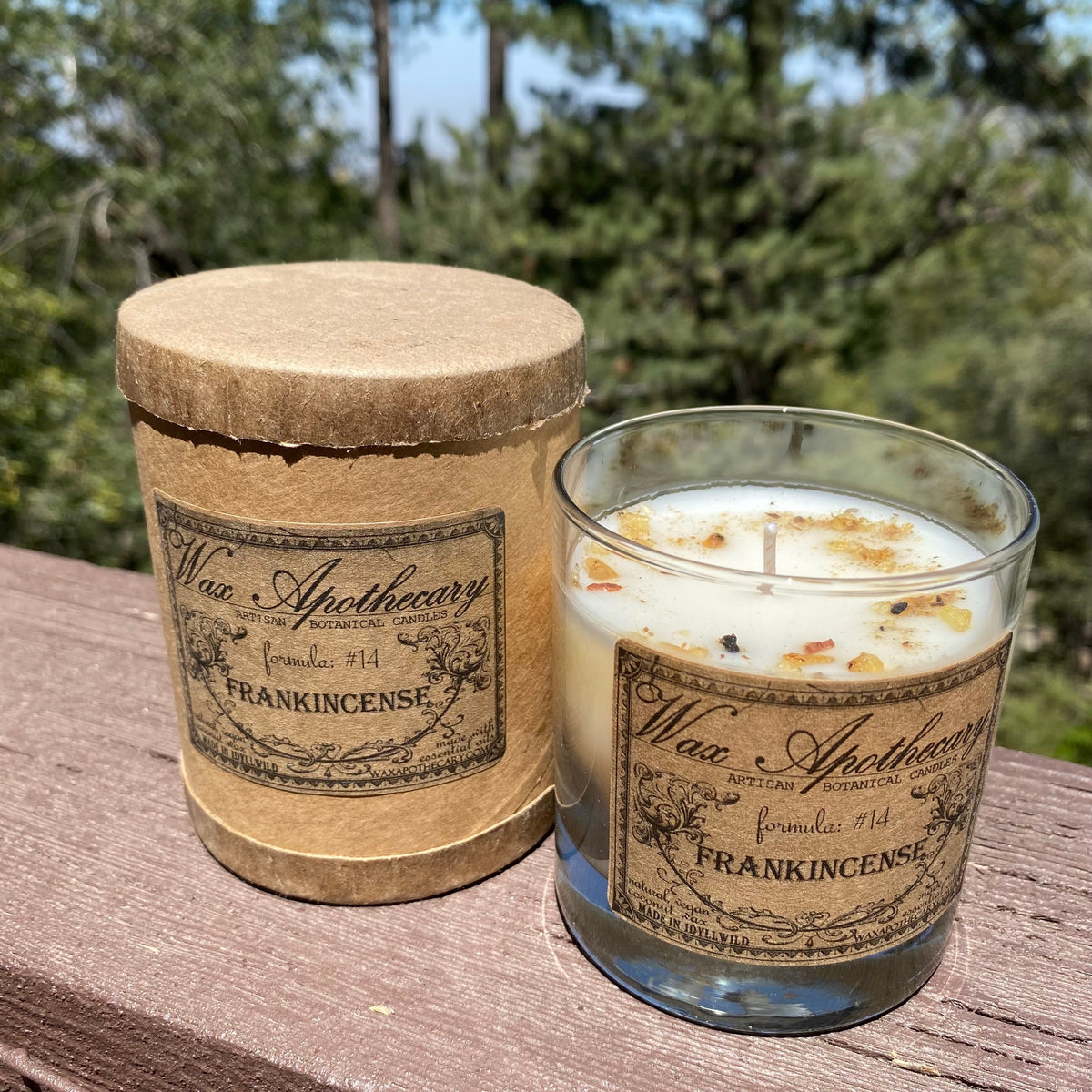 Botanical candle in clear scotch glass with Frankincense label on outdoor wooden surface