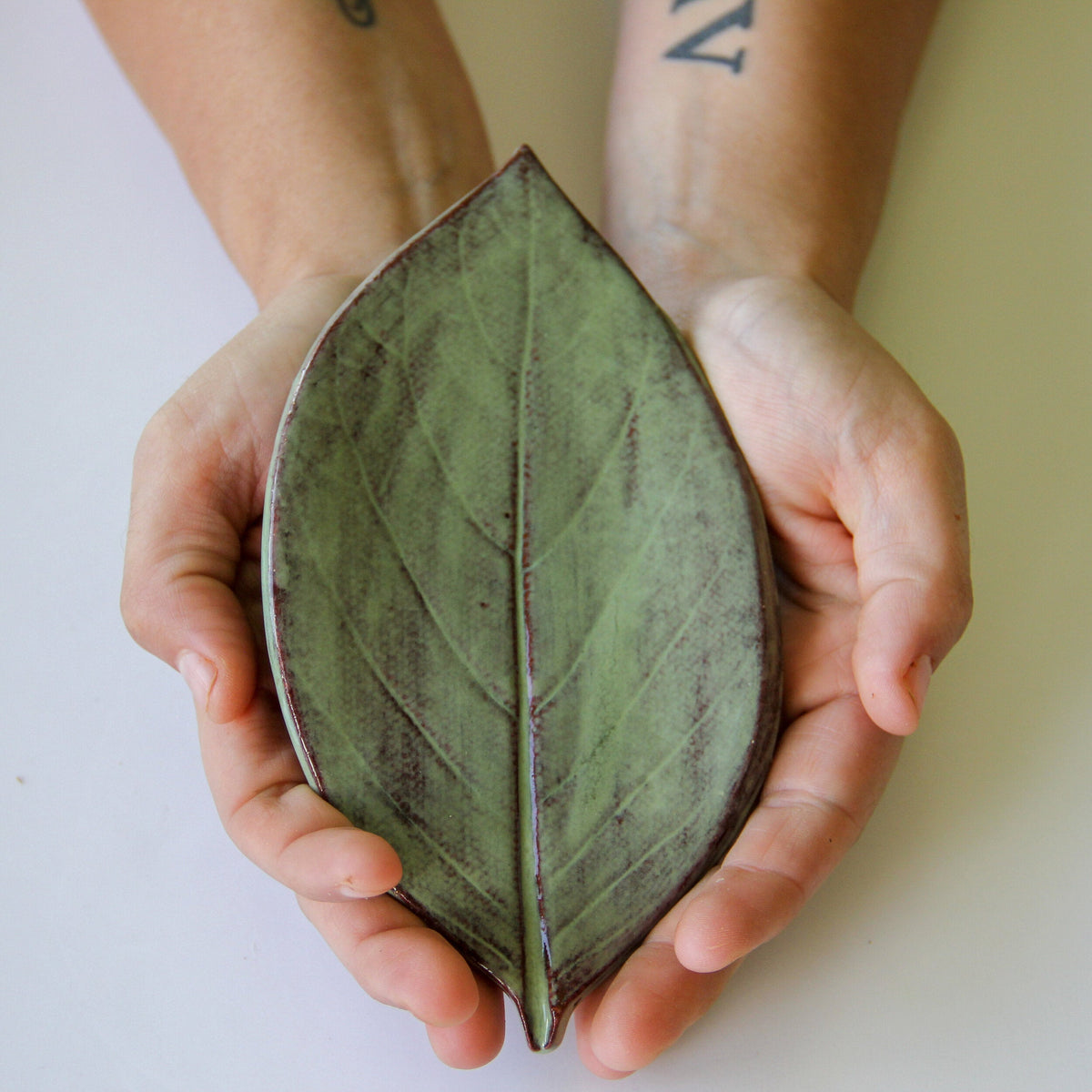 Leaf-shaped dish in moss green ceramic, held in hands for close-up view