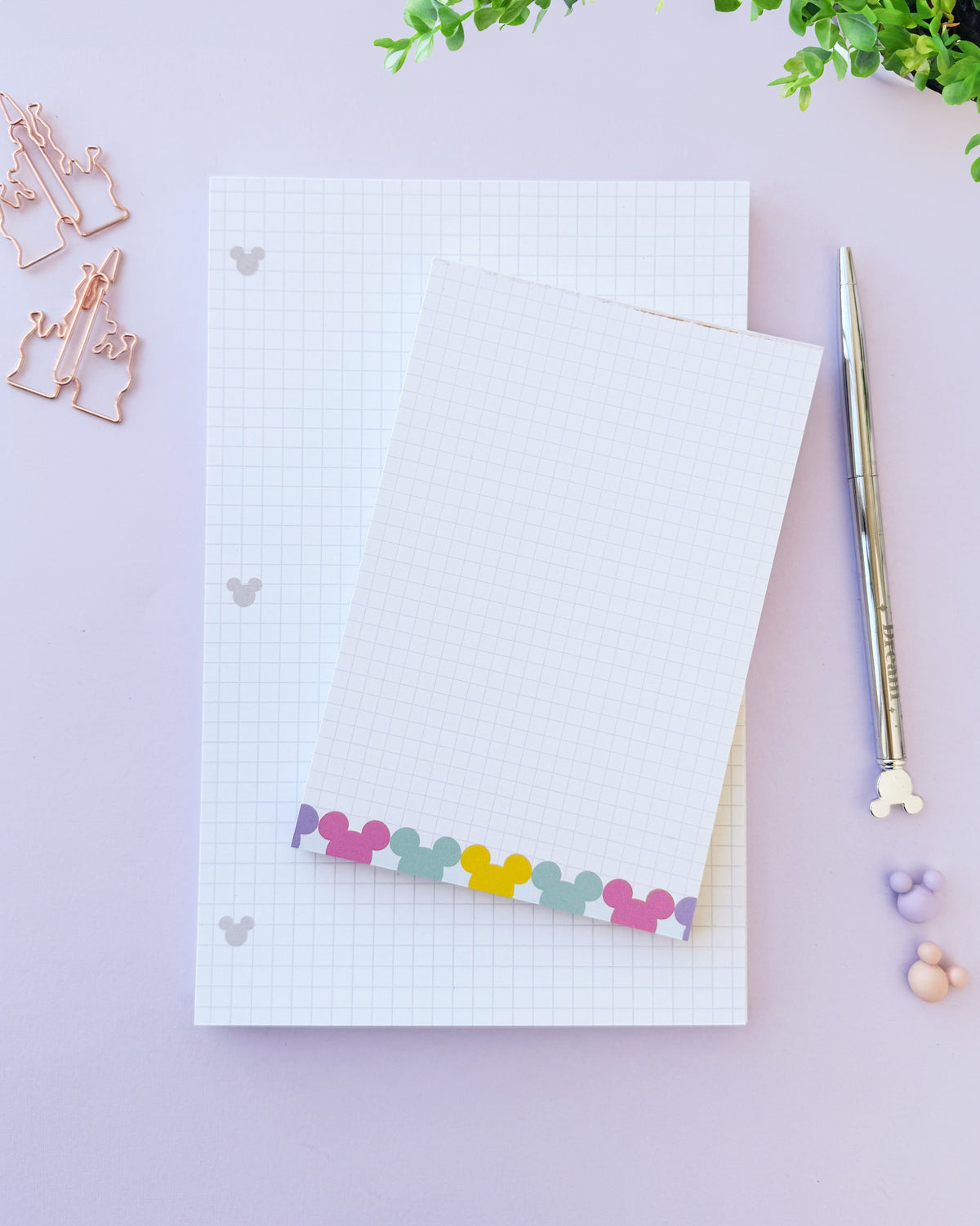 Lined paper notepad with light grid, hidden Mickey icons, and colorful bottom strip