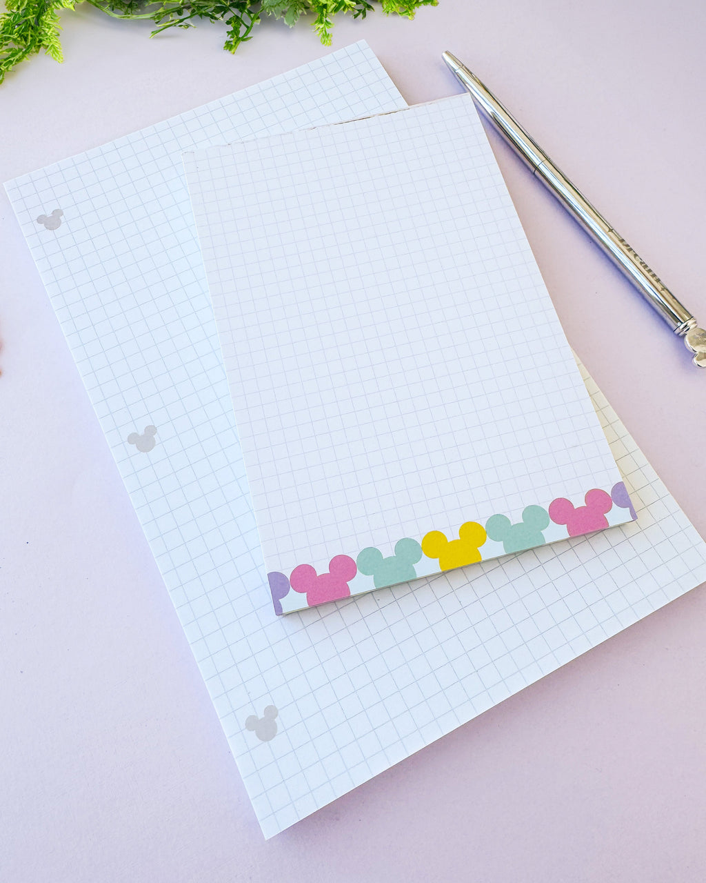 Lined paper notepad sheet with grid background, hidden Mickey icons, and rainbow strip