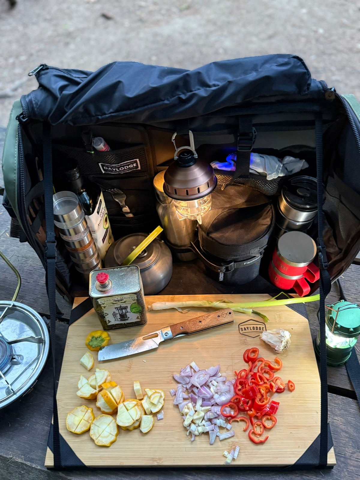 Dark navy camp kitchen table bag open with bamboo cutting board and kitchen utensils