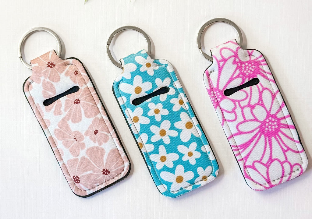 Chapstick holder keychains with pink, blue daisy, and pink botanical designs, rings