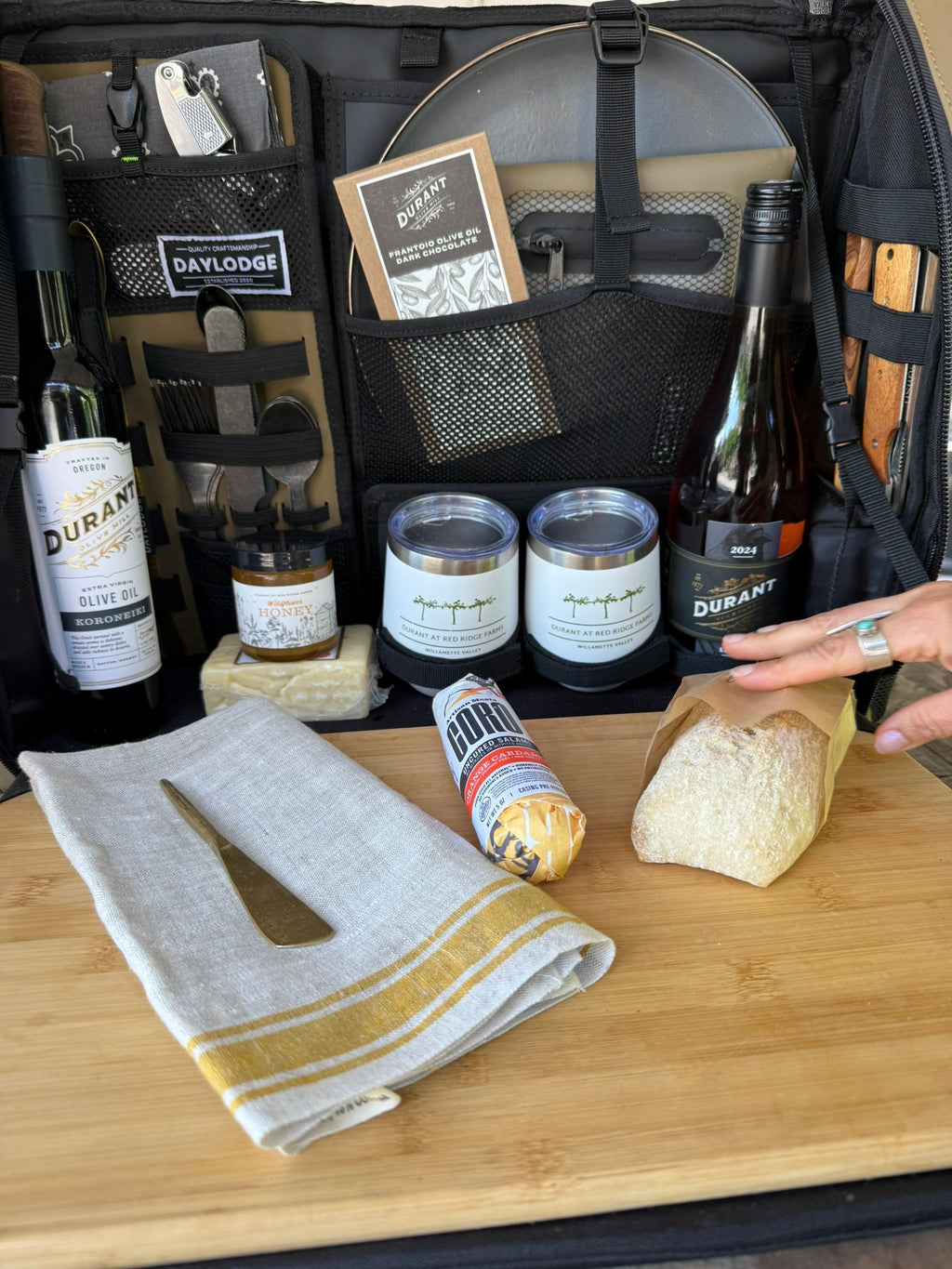 Open camp kitchen bag interior with bottles, jars, and folded cloth on bamboo board