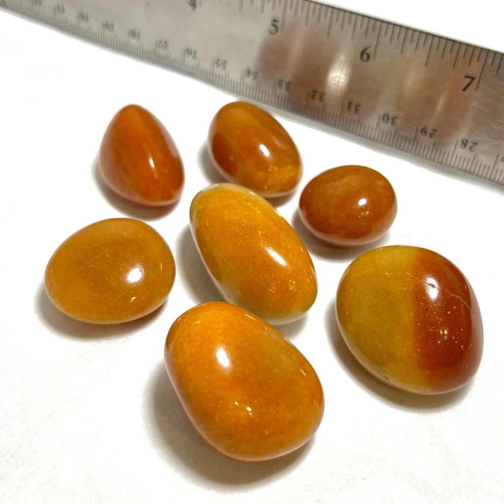 Orange aventurine tumbled stones beside a measuring ruler, glossy oval and teardrop shapes