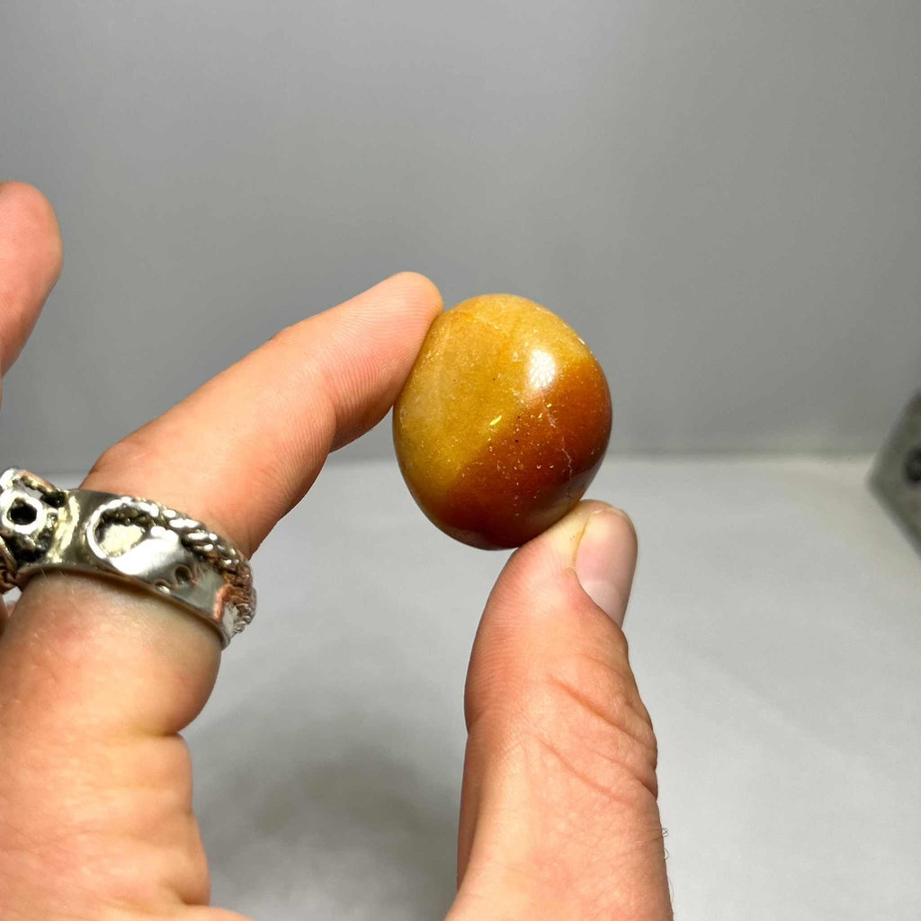 Single orange aventurine tumbled stone held between fingers, smooth glossy oval shape