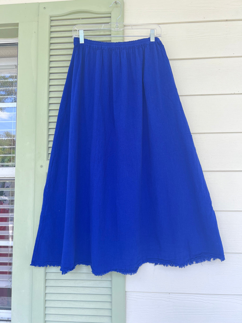 Blue cotton gauze midi skirt with elastic waistband and frayed hem, hanging