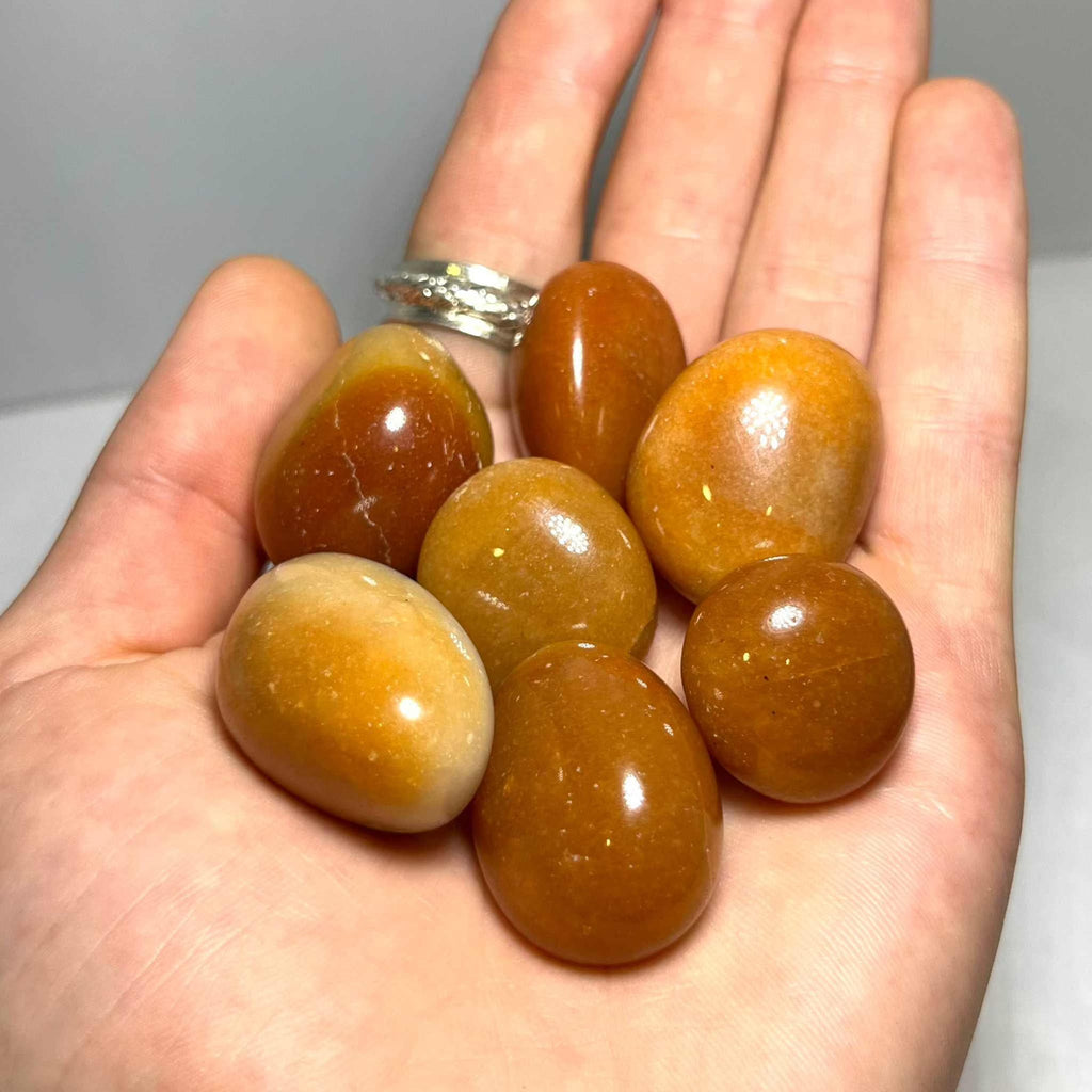 Orange aventurine tumbled stones in an open hand, smooth glossy oval and teardrop pieces
