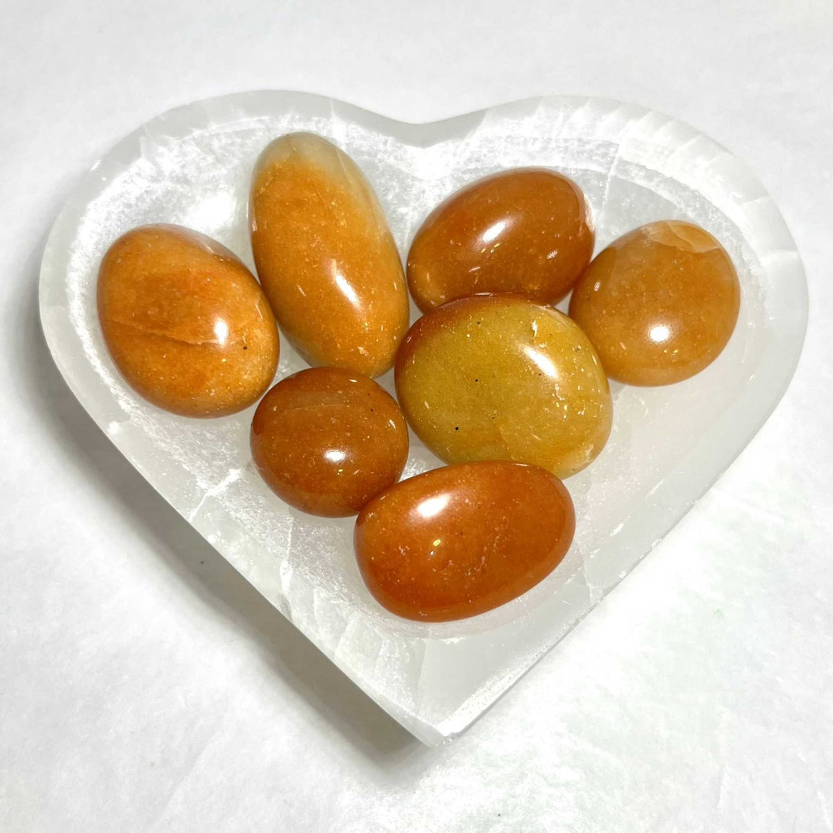 Orange aventurine tumbled stones in a white heart-shaped dish, glossy oval and teardrop pieces