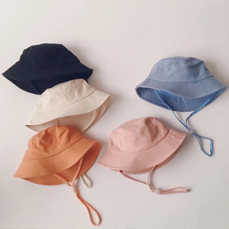 Assorted kids linen bucket hats in navy, cream, orange, pink, and light blue with chin straps