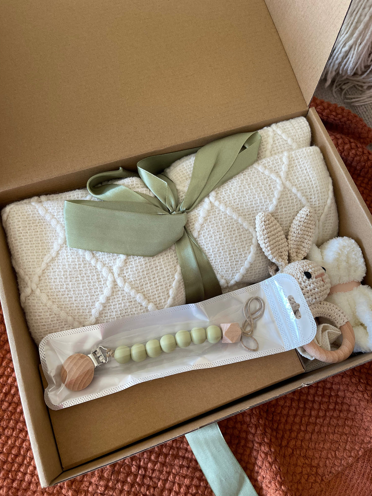 Green gift care package with folded towels, ribbon bow, and teething toy set