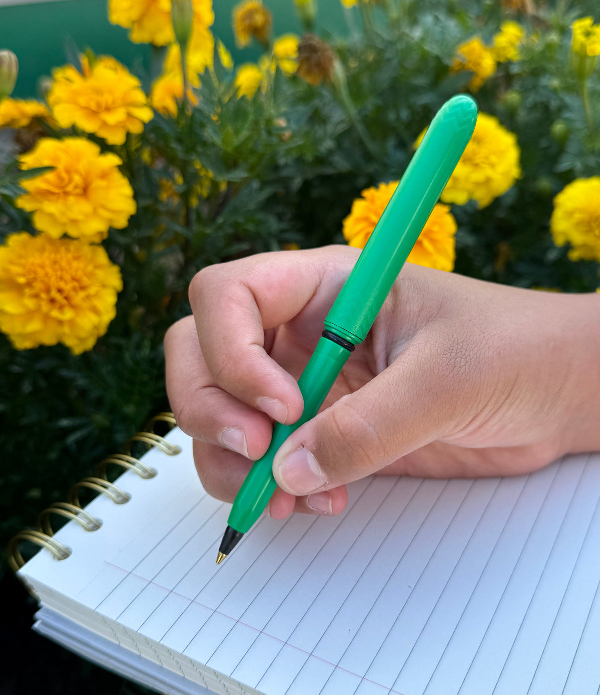 Lime green pocket pen in a hand, writing on a lined notebook