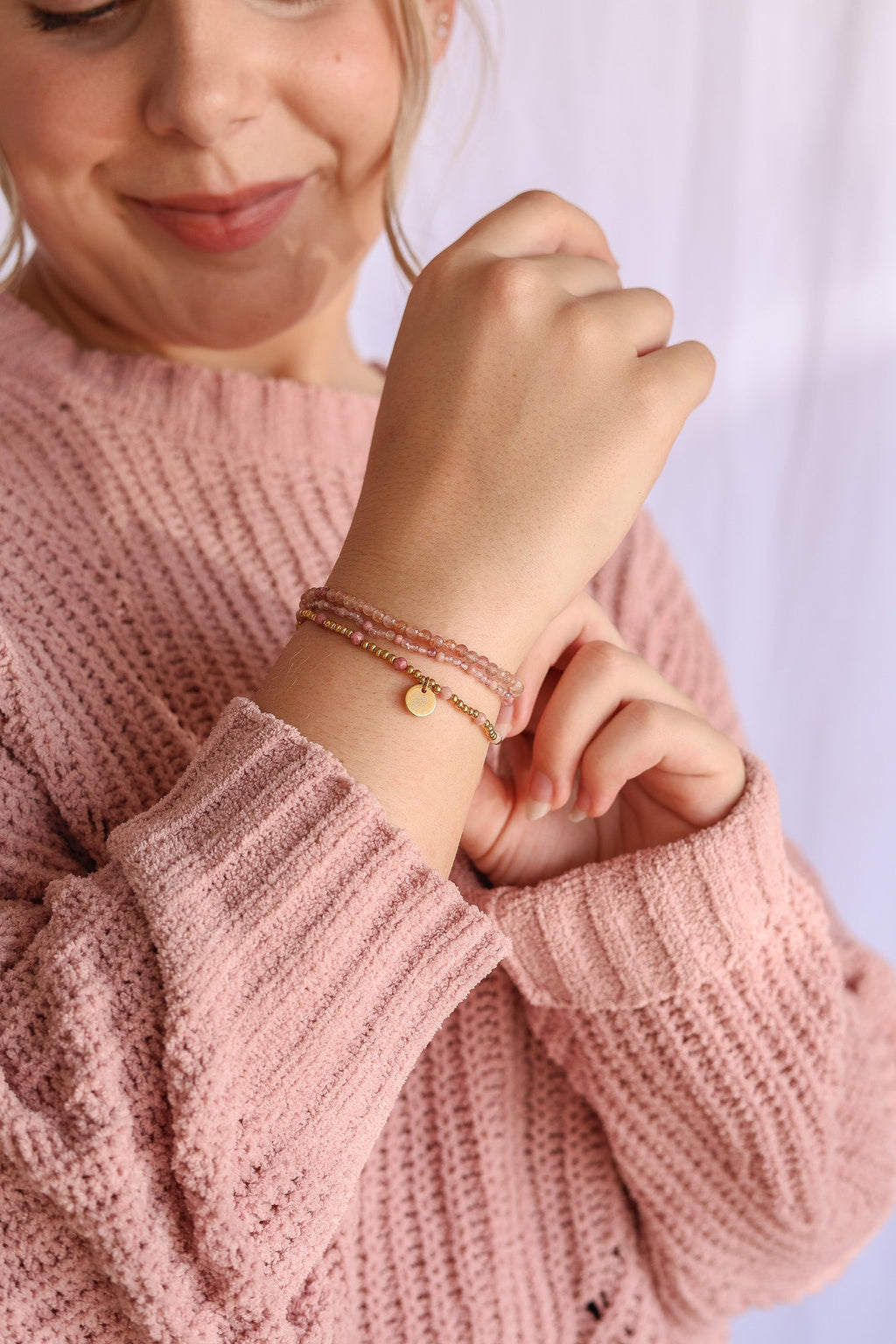 Bead stretch bracelet set on wrist with gold-tone ring clasp charm and pink beads