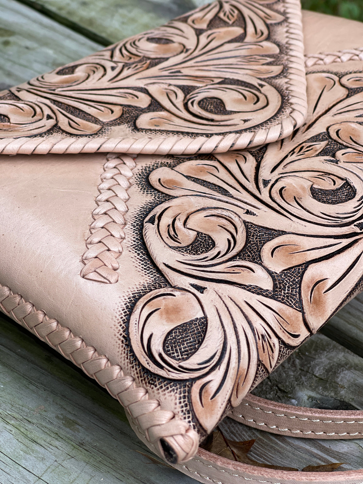 Hand-tooled leather clutch corner close-up with braided edge and floral tooling