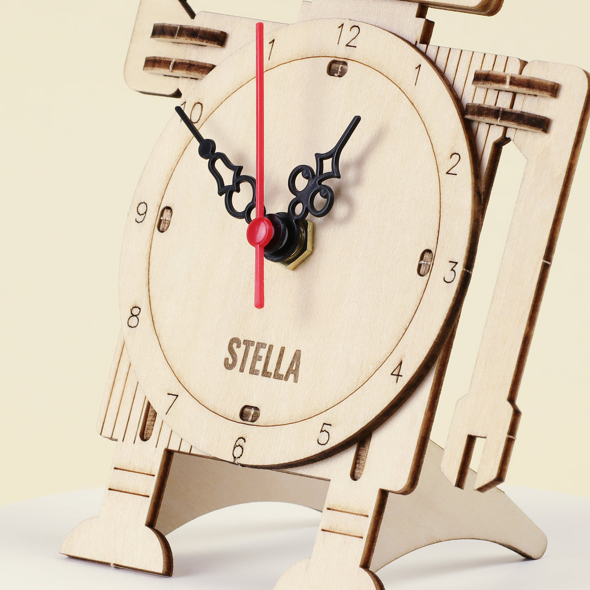 Wooden robot clock dial close-up with black hands, red second hand, and “STELLA” text