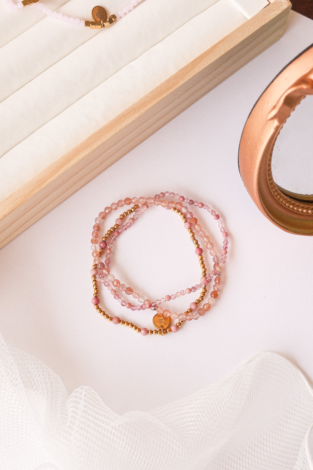 Flat lay of layered bead stretch bracelet set with pink beads and gold-tone charm