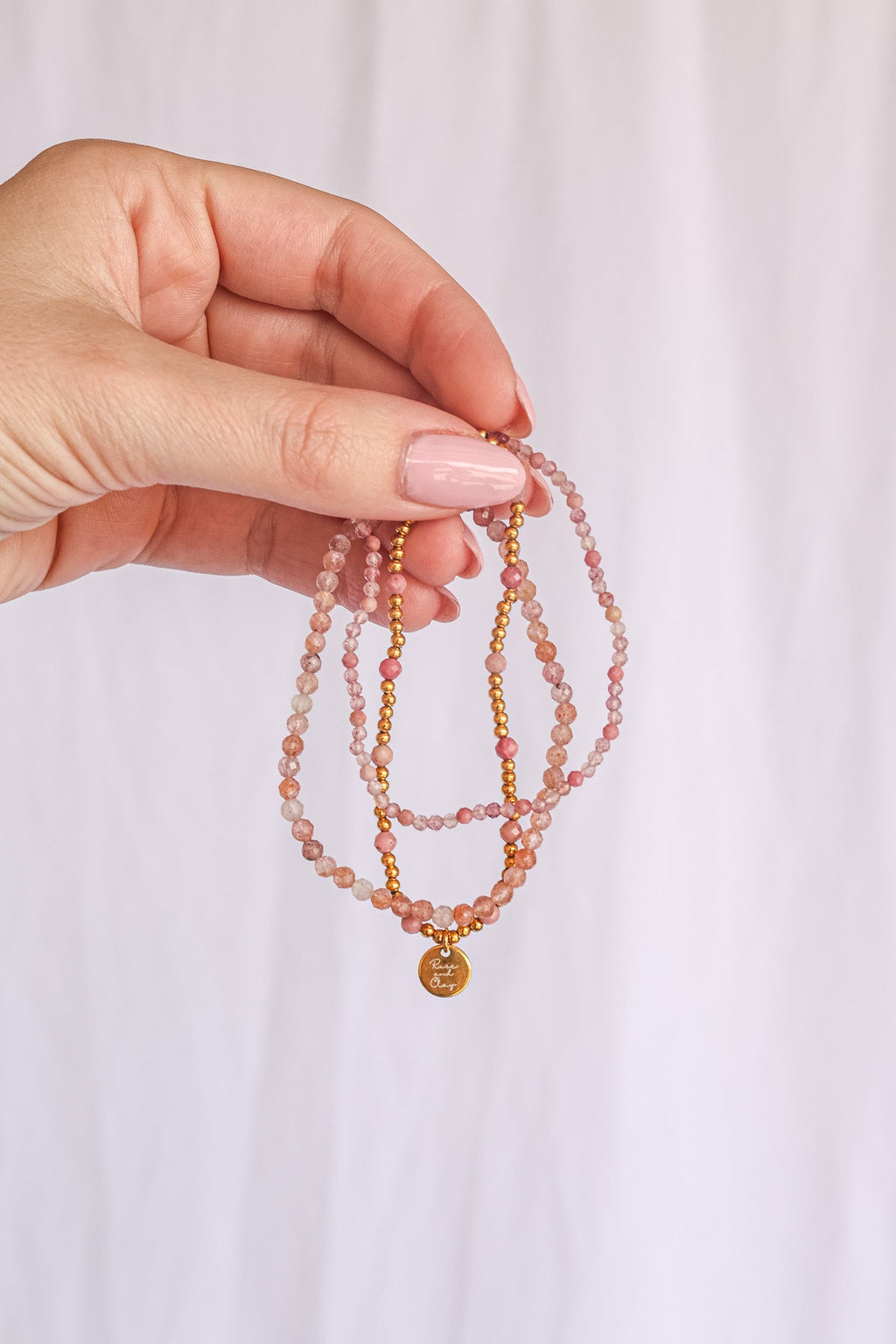 Hand holding bead stretch bracelet set with pink beads and gold-tone heart charm