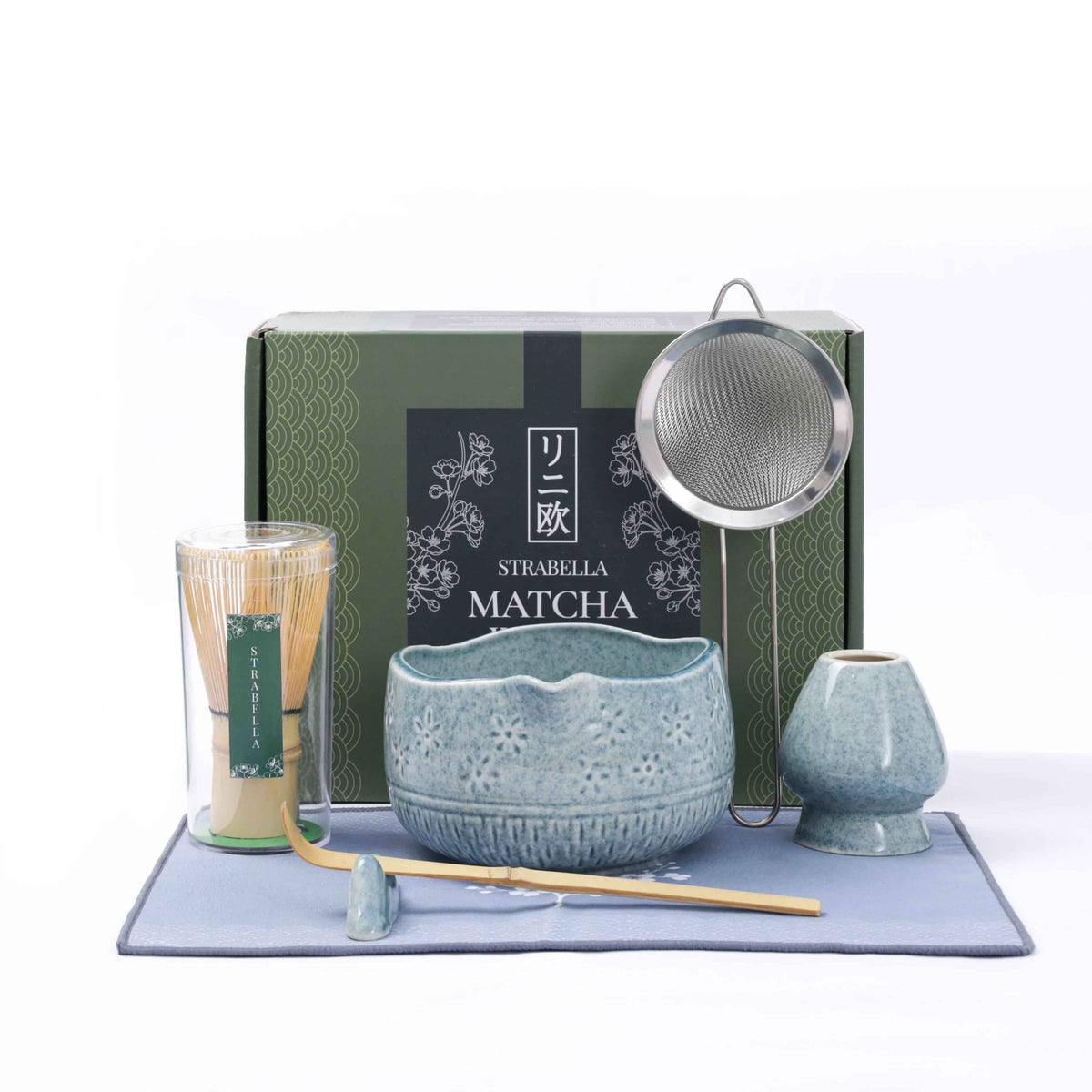 Matcha whisk set on mat with blue speckled ceramic chawan, whisk, and two small cups