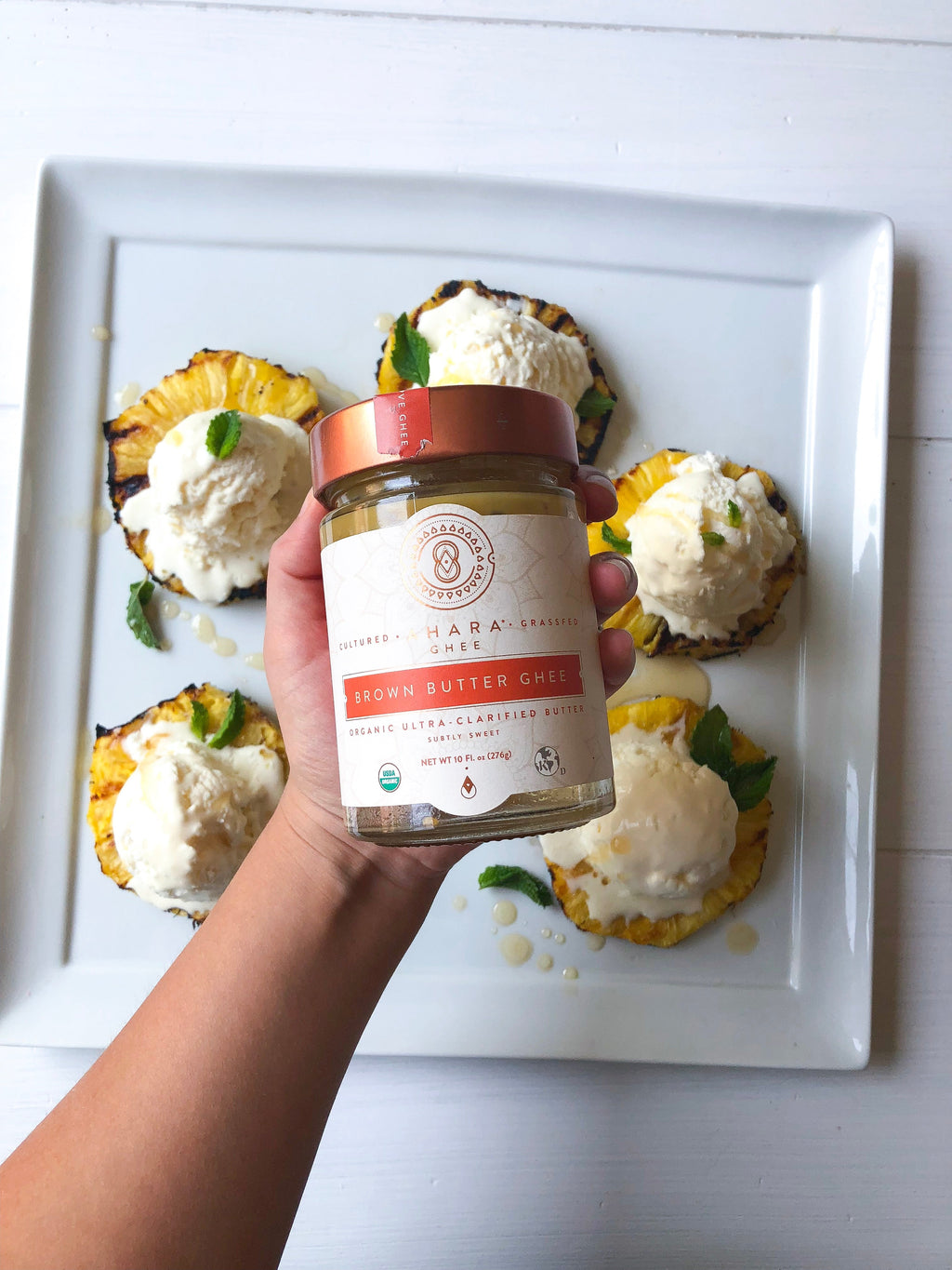 Ahara Rasa brown butter ghee jar held above white plate with dollops of ghee.