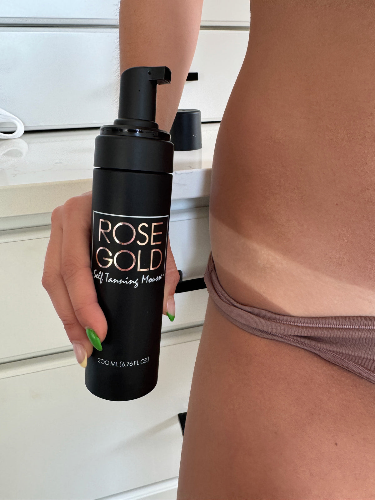 Hand holding ROSE GOLD self-tanning mousse bottle in black pump container