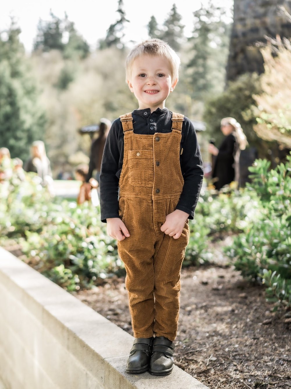Toddler barefoot sneakers, dark green, worn under brown overalls on garden steps.