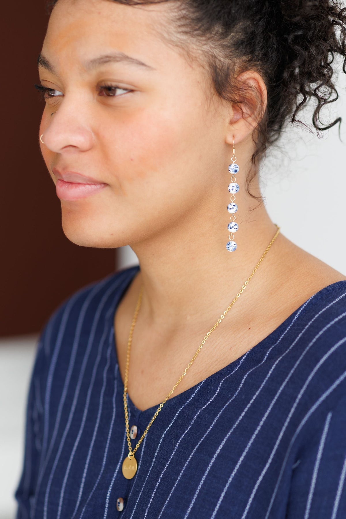 Blue porcelain bead drop earrings worn with gold chain; gold-tone hook style